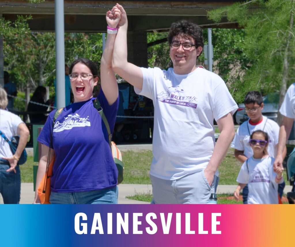 Two participants raise their joined hands and smile while walking together at the Walk the Talk epilepsy awareness event in Gainesville.
