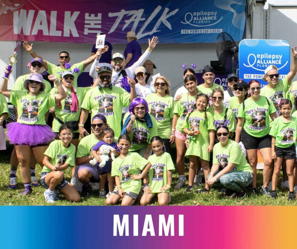 A large group of participants wearing matching shirts pose together on stage at the Walk the Talk epilepsy awareness event in Miami.